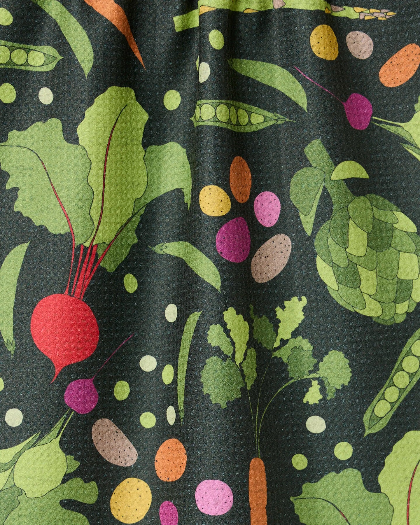 The GEOMETRY Spring Sprout tea towel features colorful vegetable illustrations—beets, carrots, peas, radishes, and artichokes—on a dark green background and is crafted from recycled materials for an eco-friendly touch.