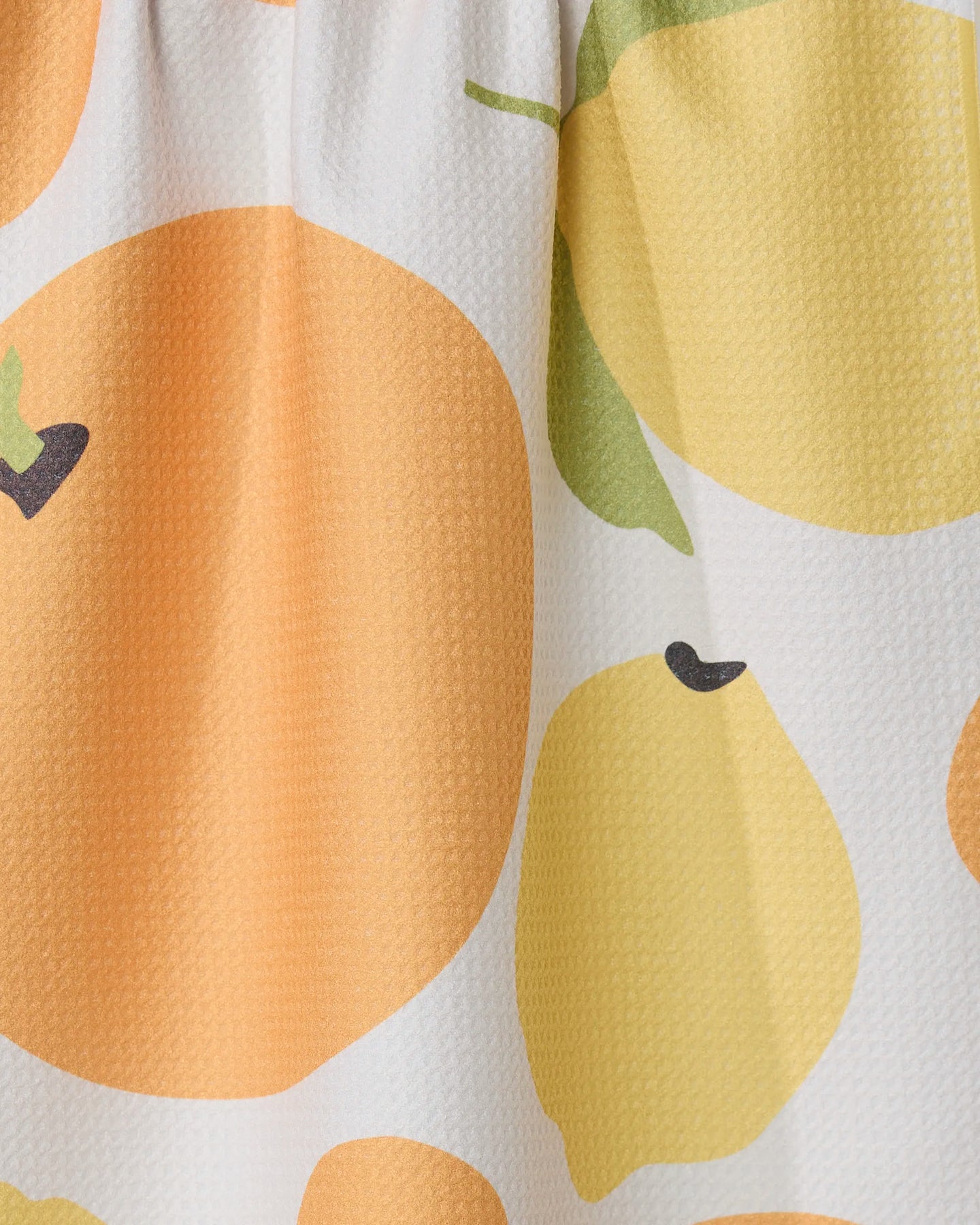 Close-up of GEOMETRYs Sunny Lemons And Oranges recycled kitchen towel, featuring bright orange and yellow fruit shapes with green leaves and black stems on a white background.