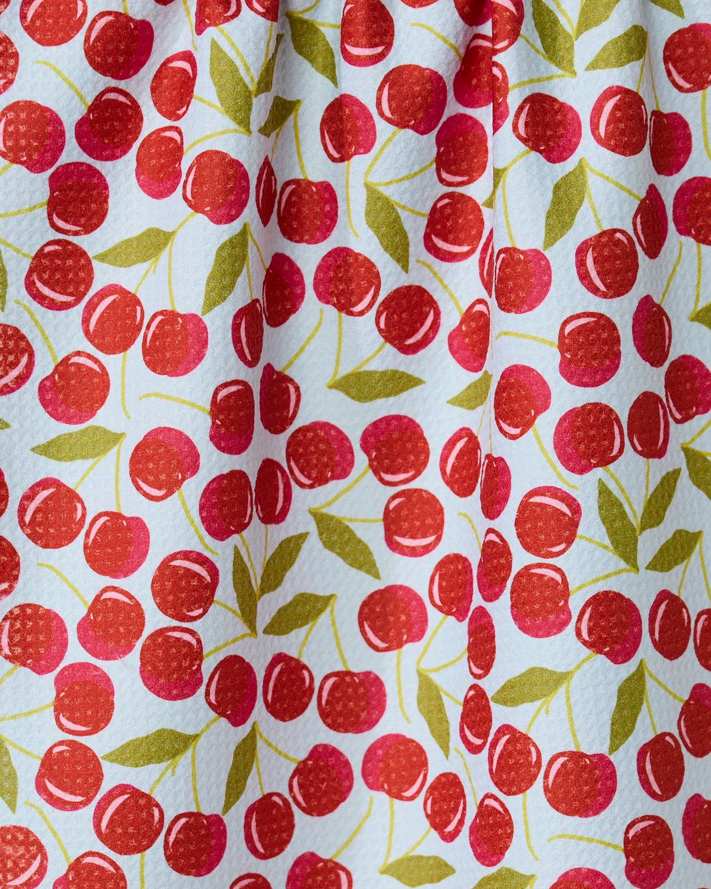 The GEOMETRY Sweet Cherry towel features a colorful cherry pattern with red cherries and green leaves on white. Quick-drying and slightly textured, it’s gathered at the top, perfect for adding a cheerful touch to your kitchen.