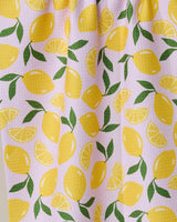 The GEOMETRY Sweet Lemon tea towel features whole yellow lemons, lemon slices, and green leaves on a light pink background. This charming, absorbent dish towel with a textured surface adds style and function to your kitchen.