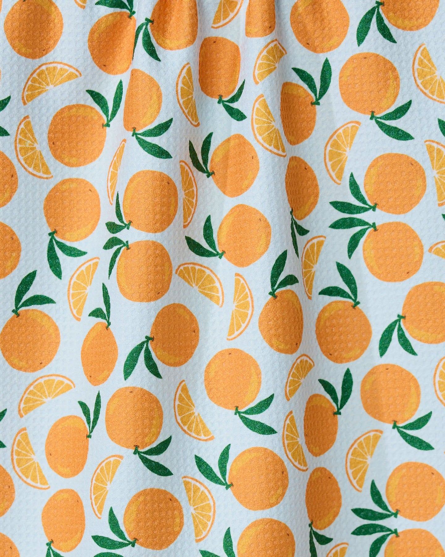 The GEOMETRY Sweet Orange tea towel features vibrant illustrations of whole oranges, slices, and green leaves on textured white fabric, adding both style and practicality to your kitchen.