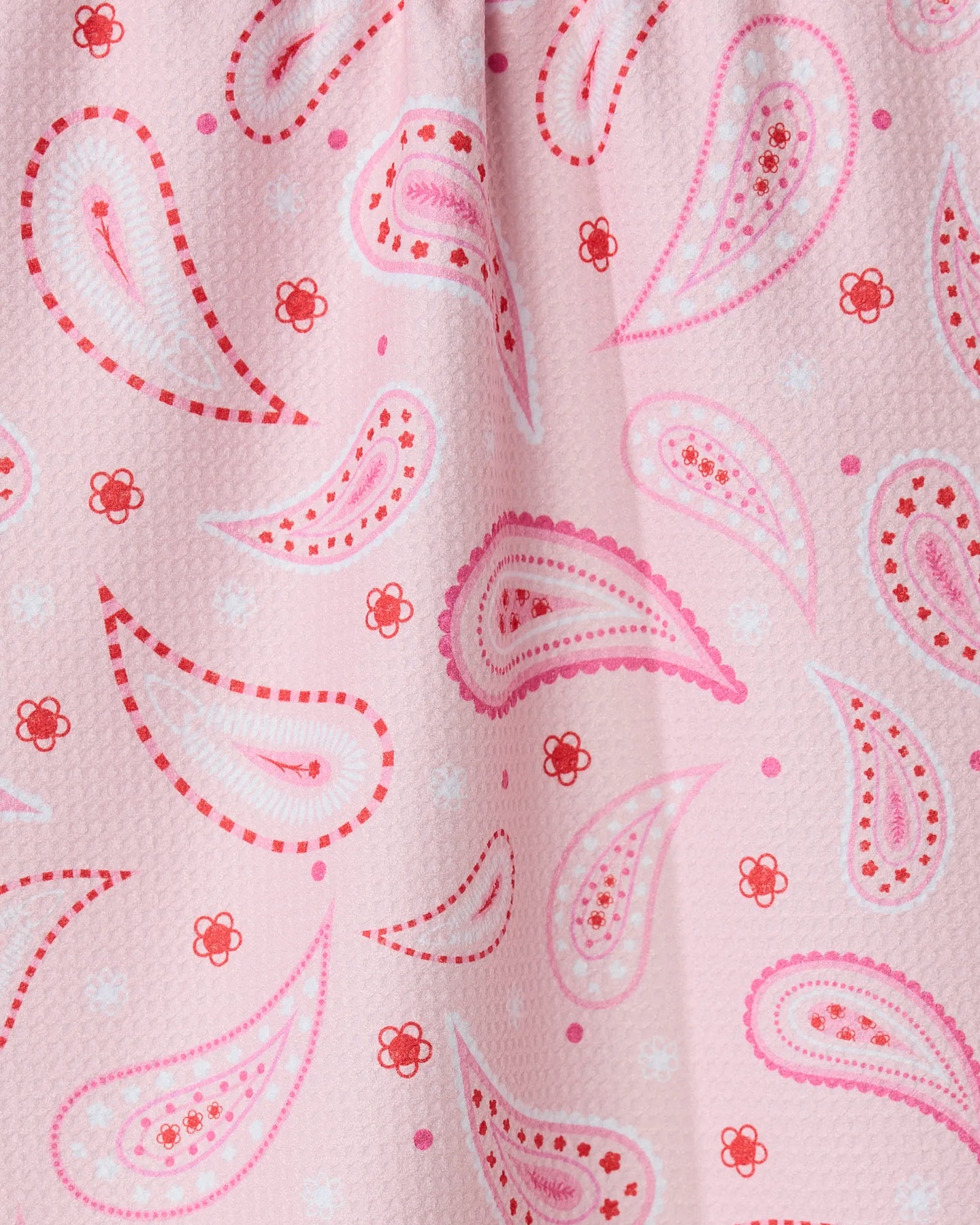 Close-up of the Sweet Paisley tea towel by GEOMETRY, featuring a pink paisley pattern with red and white accents, teardrop and flower motifs. Made from quick-drying, recycled materials with visible folds and texture.