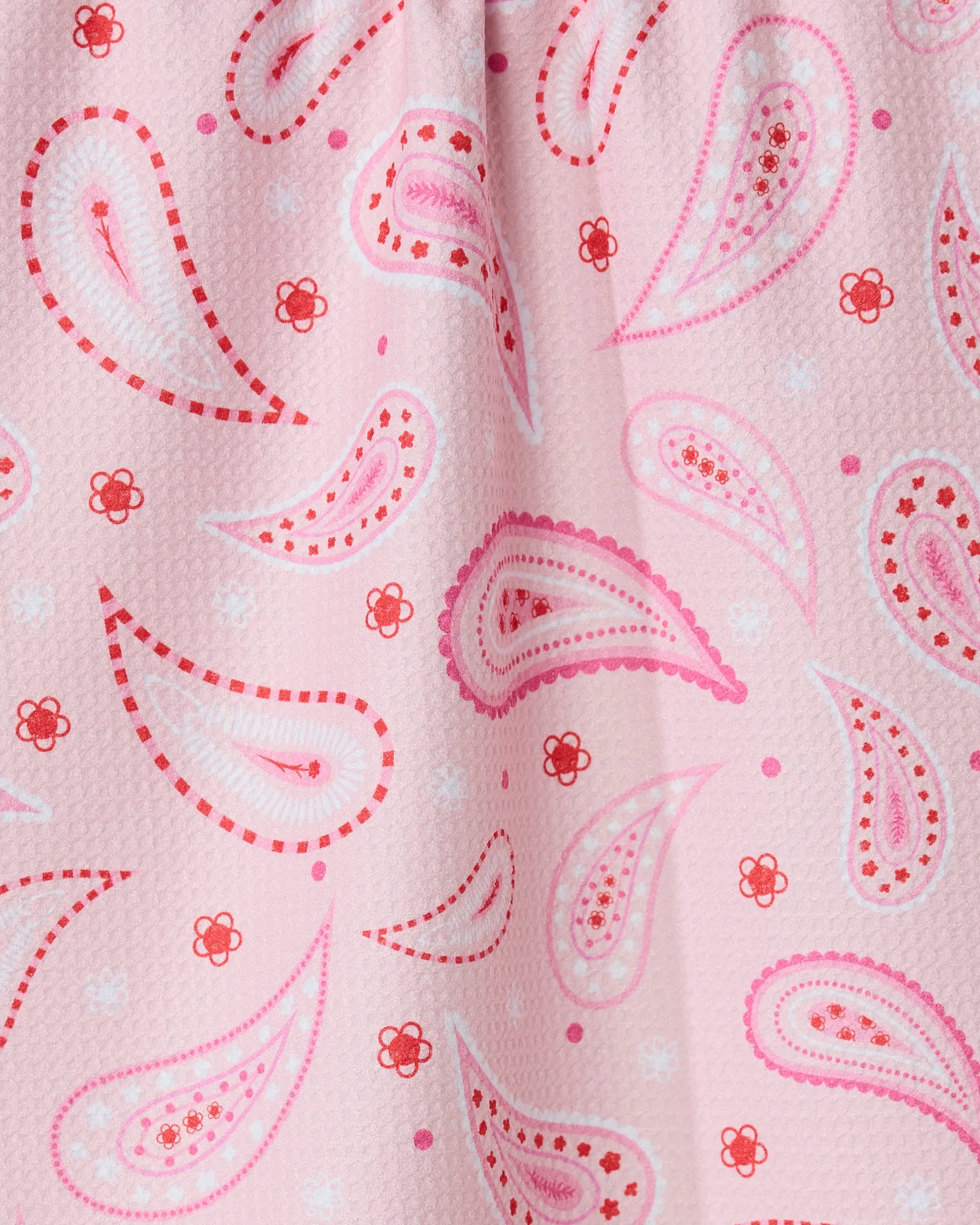 Close-up of the Sweet Paisley tea towel by GEOMETRY, featuring a pink paisley pattern with red and white accents, teardrop and flower motifs. Made from quick-drying, recycled materials with visible folds and texture.