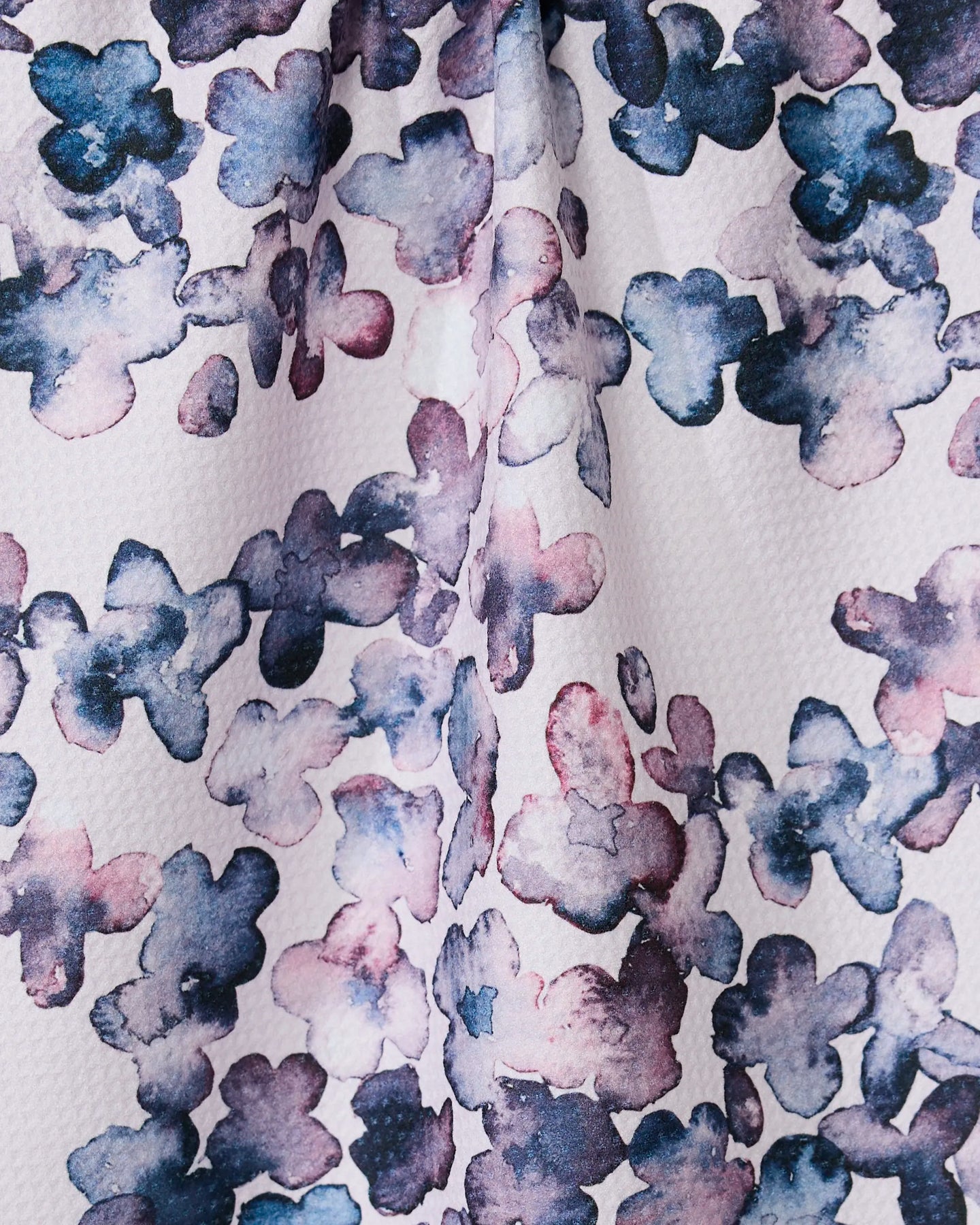 The GEOMETRY Sweet Petals tea towel showcases a blue, purple, and pink abstract floral watercolor pattern on textured white, crafted from ultra-absorbent recycled materials.