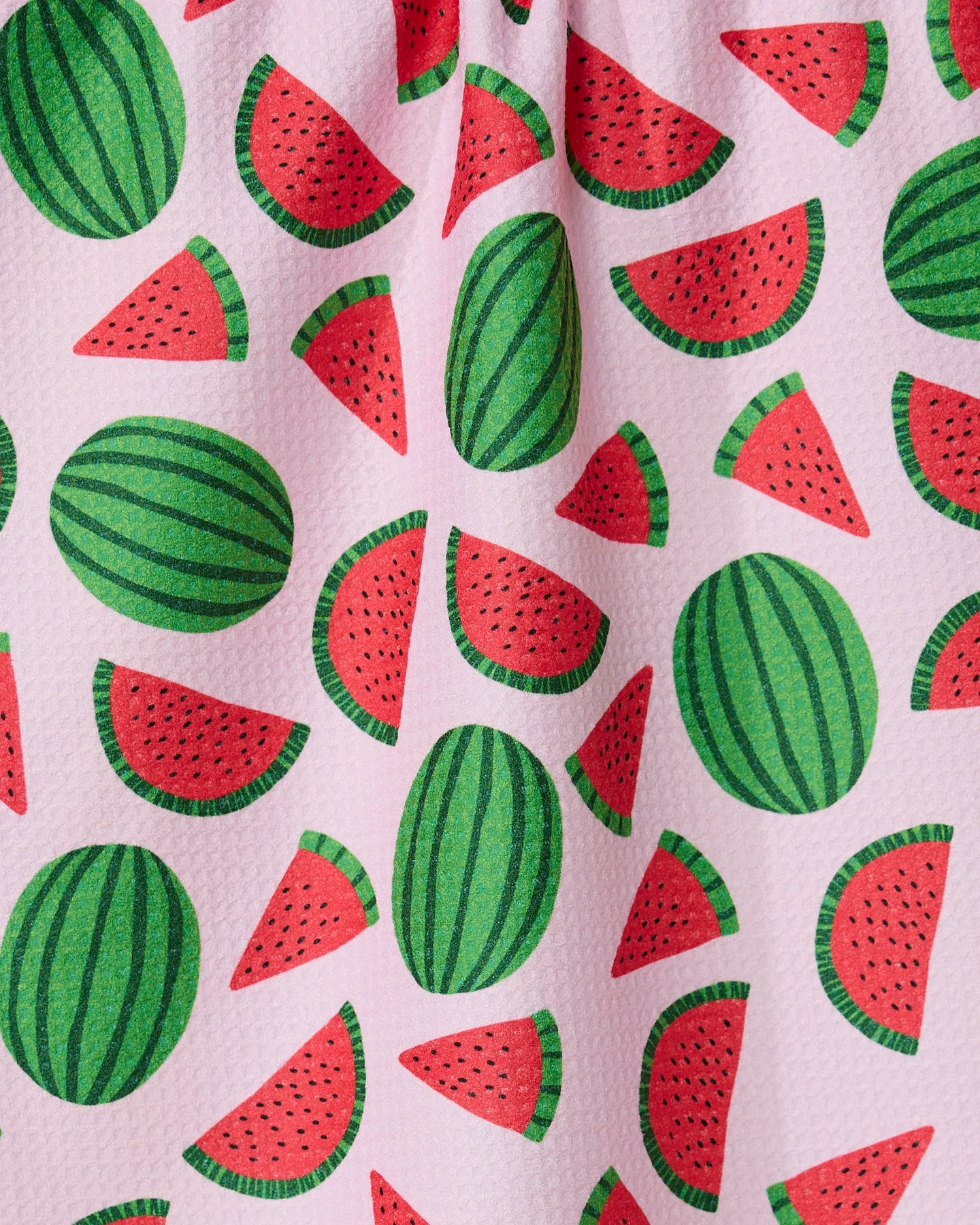 The GEOMETRY Sweet Watermelon kitchen tea towel has a pink textured surface with a playful green and red watermelon and slice pattern scattered across it.