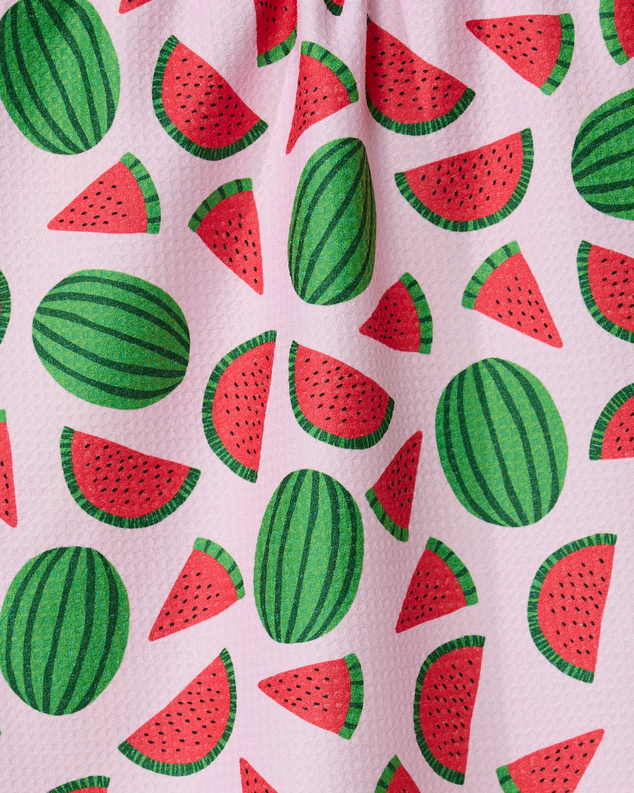 The GEOMETRY Sweet Watermelon kitchen tea towel has a pink textured surface with a playful green and red watermelon and slice pattern scattered across it.