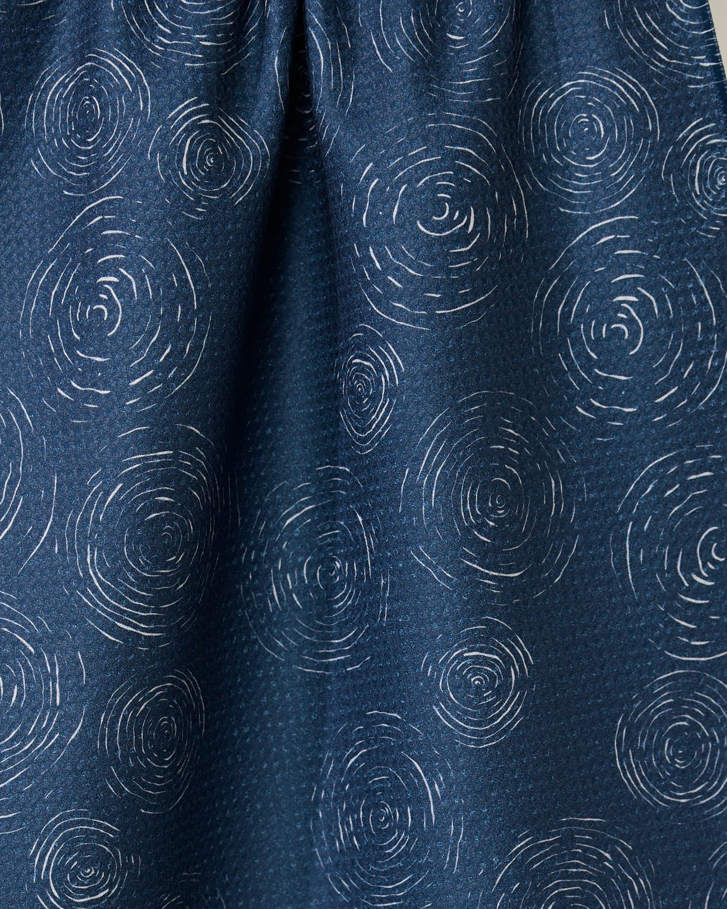 Close-up of the GEOMETRY Taps - Midnight towel, featuring a dark blue quick-drying fabric with light, circular concentric line patterns resembling ripples or tree rings scattered across the surface.
