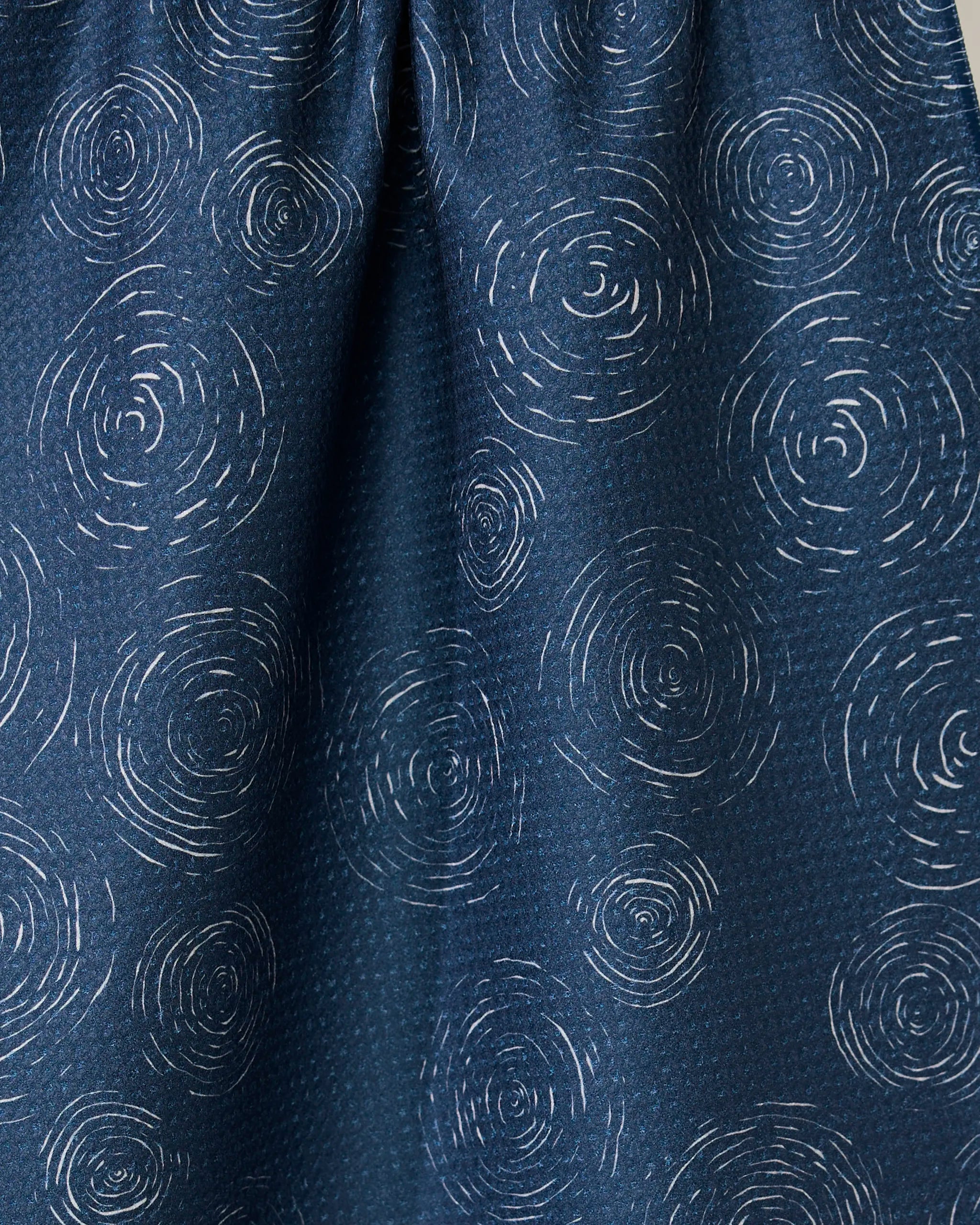 Close-up of the GEOMETRY Taps - Midnight towel, featuring a dark blue quick-drying fabric with light, circular concentric line patterns resembling ripples or tree rings scattered across the surface.