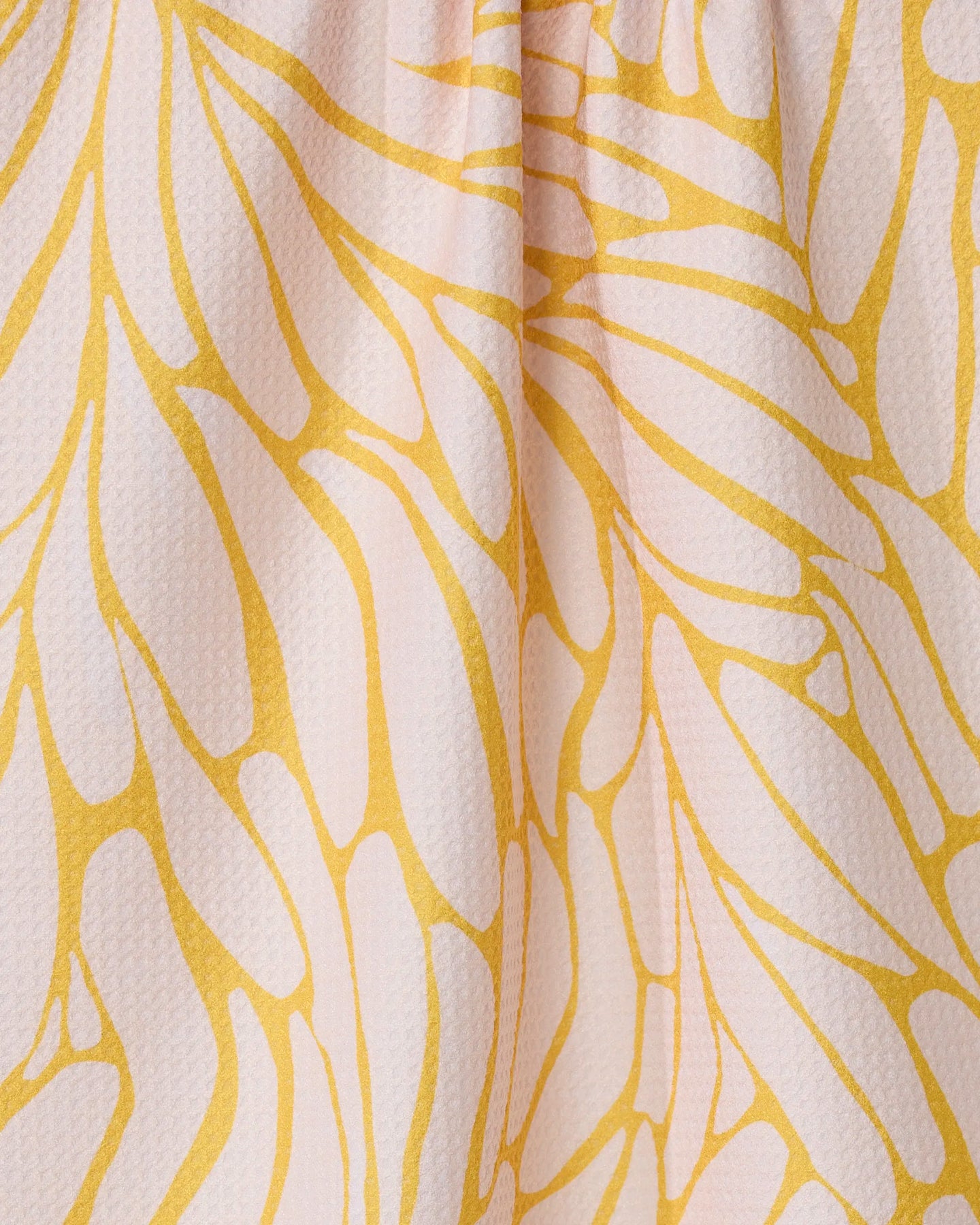 Close-up of GEOMETRY’s Tenderhearted: a quick-drying tea towel made from recycled materials, featuring a textured surface and an abstract yellow-and-white leaf pattern, softly gathered for added depth.