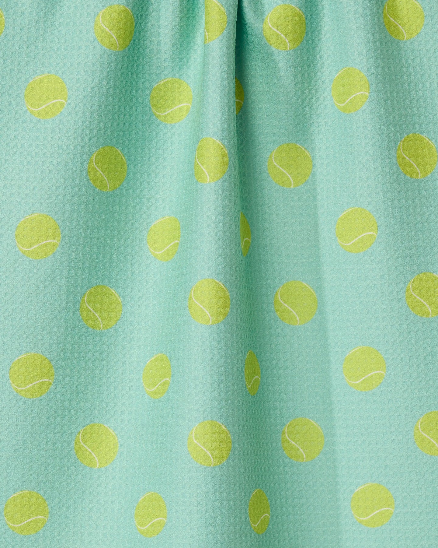 The GEOMETRY Tennis Ball kitchen towel is aqua-colored, eco-friendly, and patterned with yellow tennis balls. It features a slightly textured surface with subtle fabric folds.