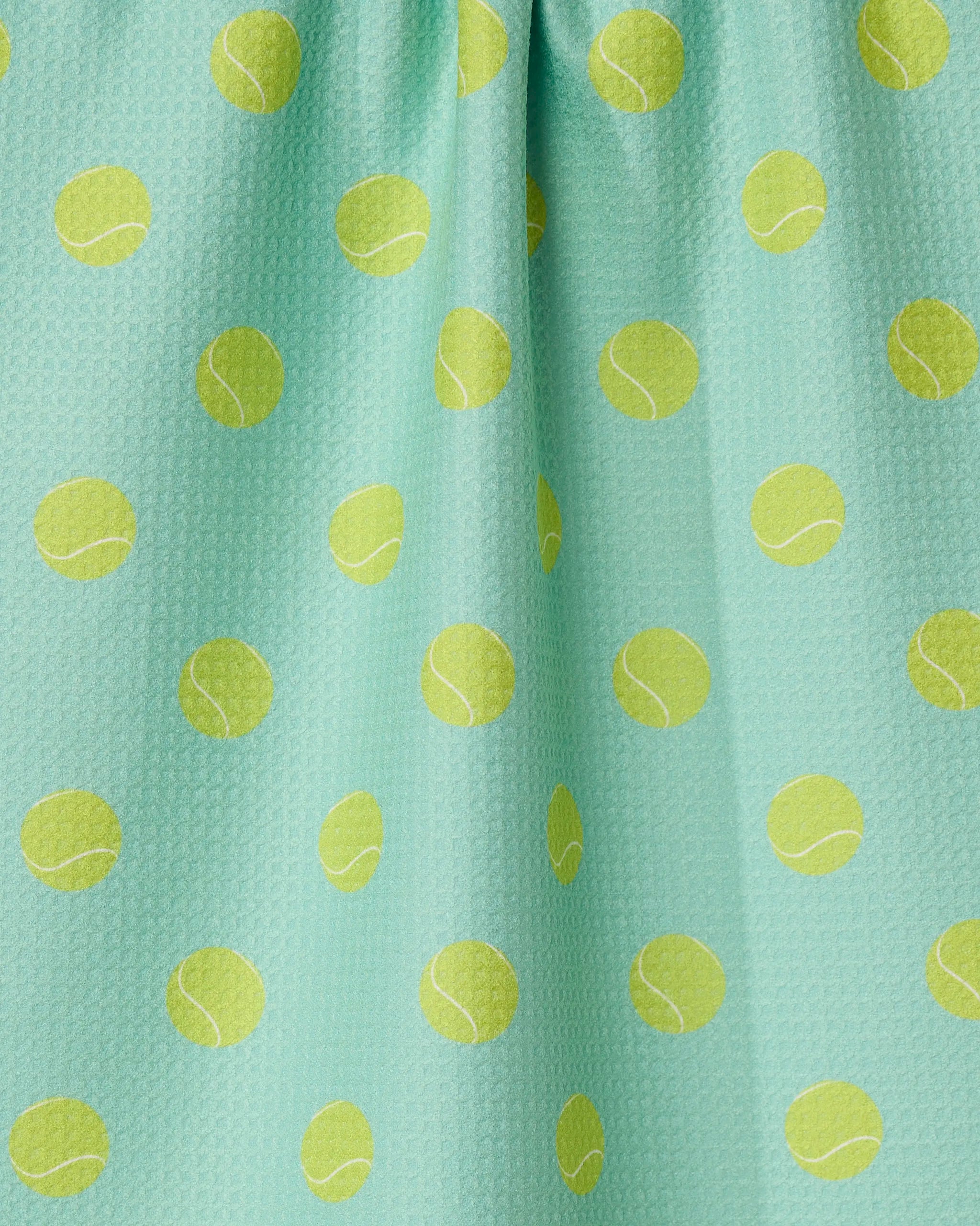 The GEOMETRY Tennis Ball kitchen towel is aqua-colored, eco-friendly, and patterned with yellow tennis balls. It features a slightly textured surface with subtle fabric folds.