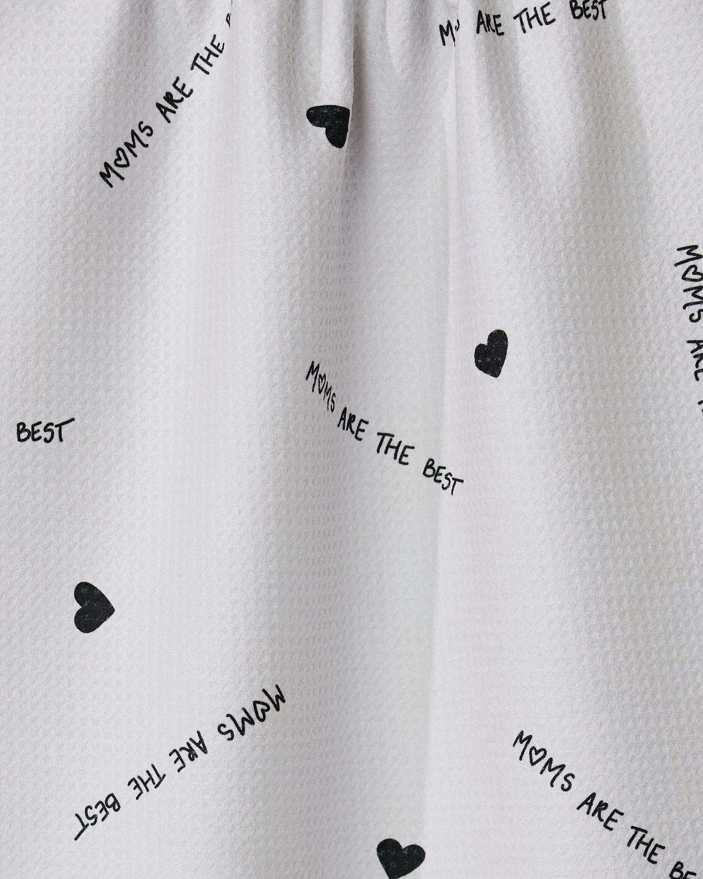 The Best tea towel by GEOMETRY features white textured fabric with small black hearts and scattered MOMS ARE THE BEST text. Made from recycled materials, its eco-friendly and ultra-absorbent.