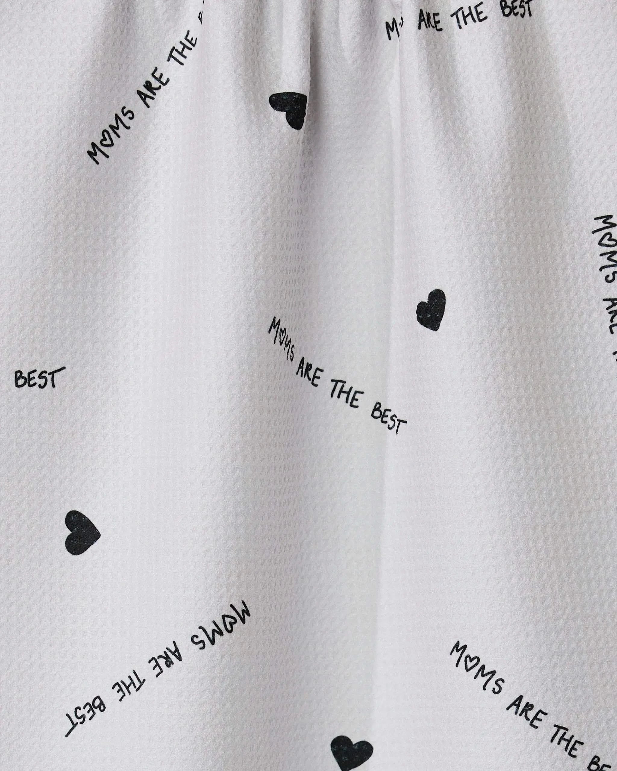The Best tea towel by GEOMETRY features white textured fabric with small black hearts and scattered MOMS ARE THE BEST text. Made from recycled materials, its eco-friendly and ultra-absorbent.