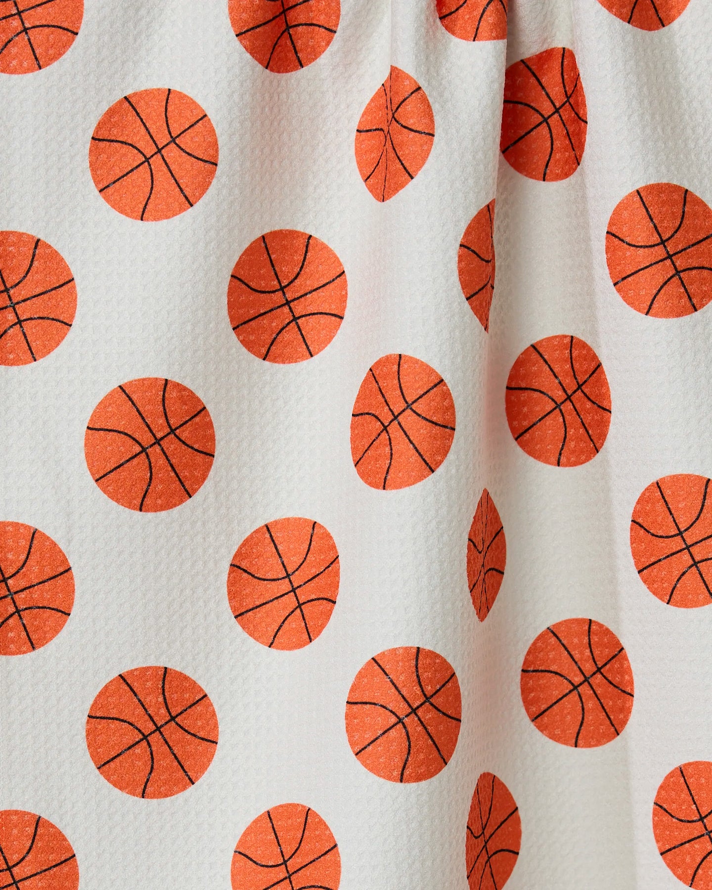 The Three Pointer by GEOMETRY is a white tea towel made from recycled materials, featuring a textured surface with an all-over orange basketball and black line pattern plus gentle folds for added depth.