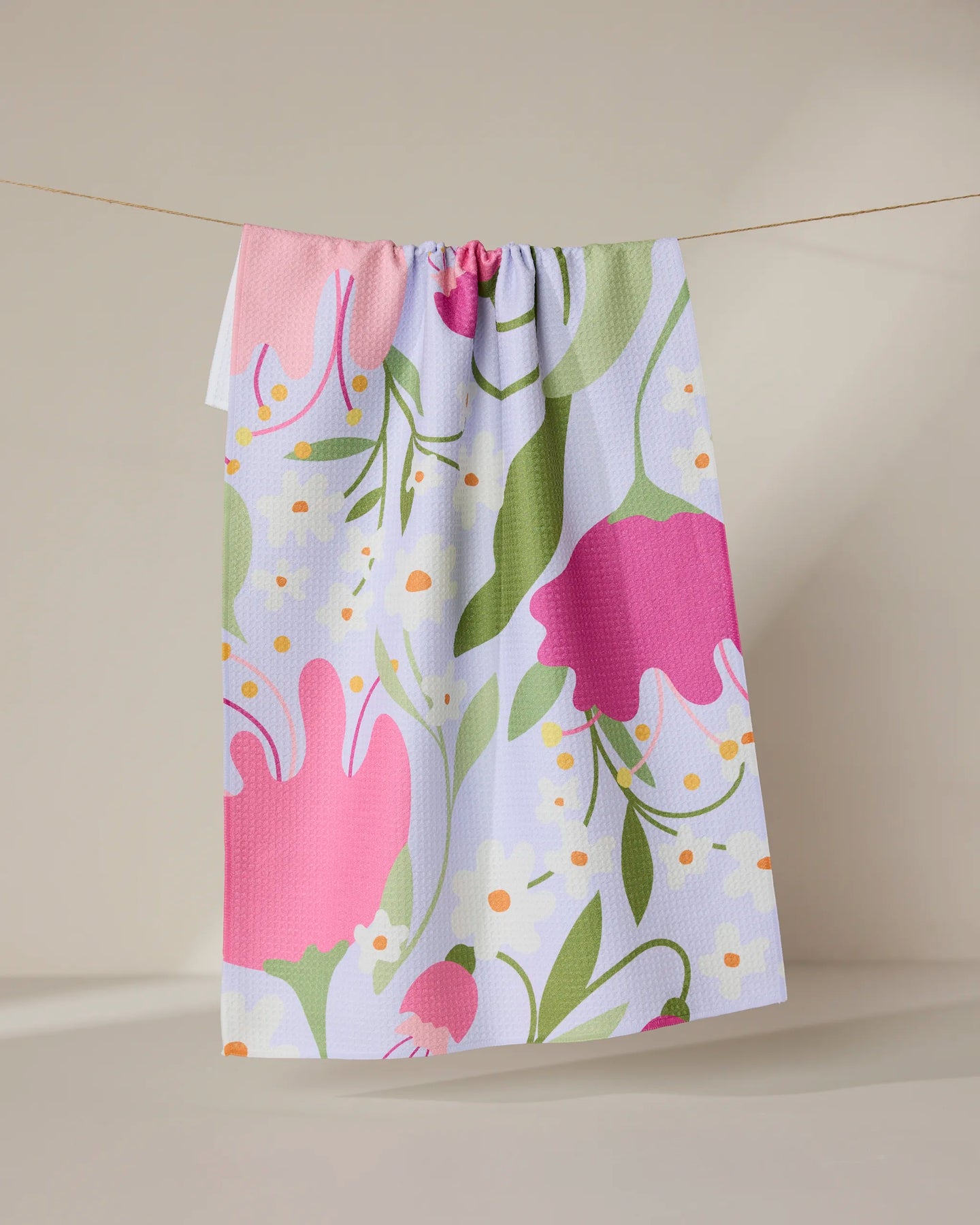 The GEOMETRY Thoughtful tea towel, made from recycled materials, features a vibrant floral design with large pink and red flowers, green leaves, and yellow-white accents. It hangs on a beige background and dries quickly.