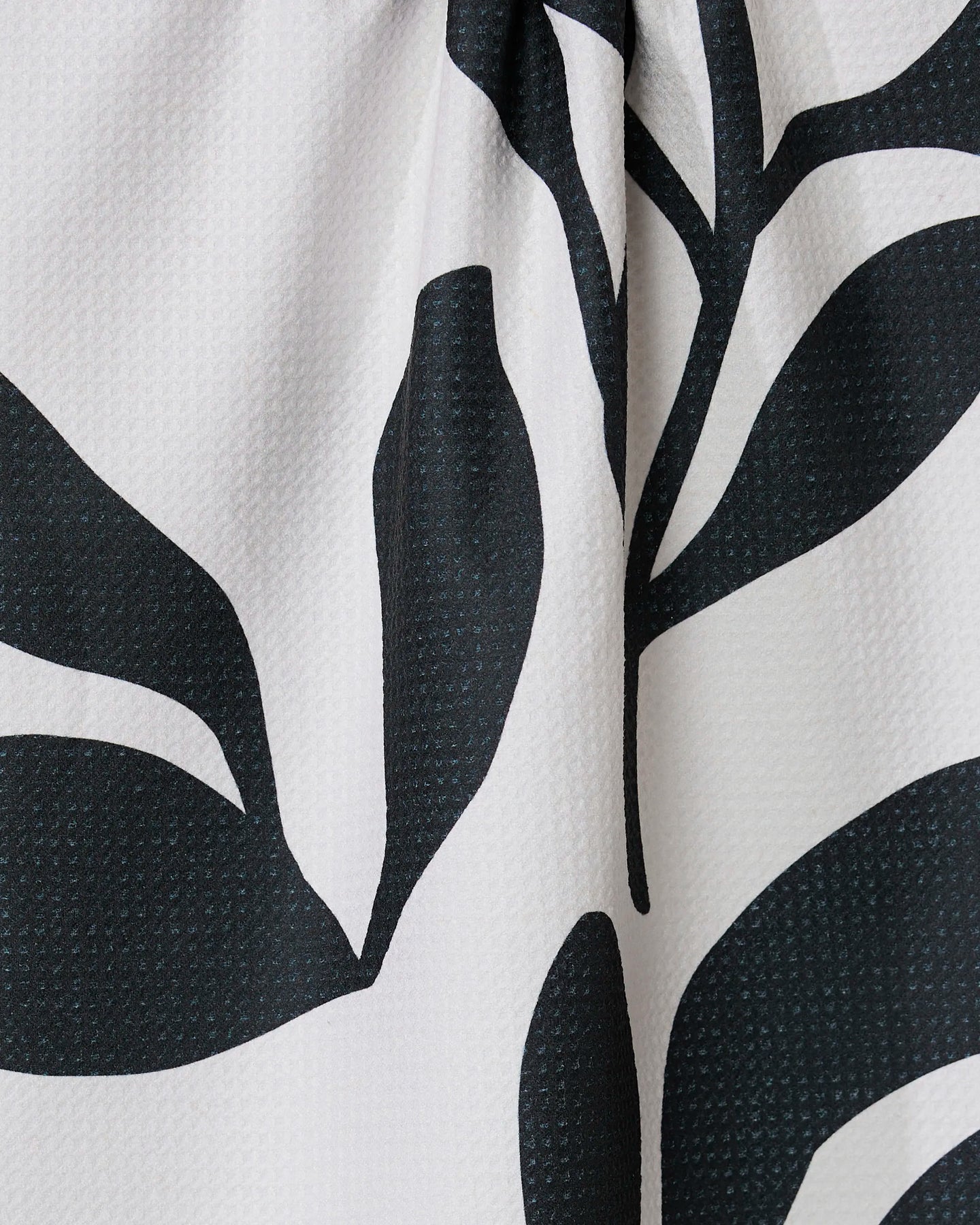 Close-up of the Threes tea towel by GEOMETRY, ultra-absorbent and made from recycled materials, featuring a bold black and white abstract leaf pattern on a textured light background.