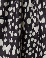 Close-up of Geometrys Cass tea towel in black with irregular white spots, resembling an abstract animal print. A small black tag is visible—this quick-drying towel brings bold style to any kitchen.