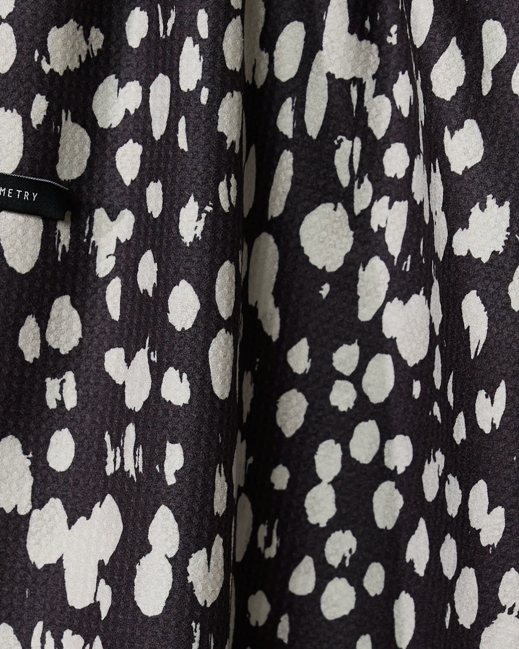 Close-up of Geometrys Cass tea towel in black with irregular white spots, resembling an abstract animal print. A small black tag is visible—this quick-drying towel brings bold style to any kitchen.