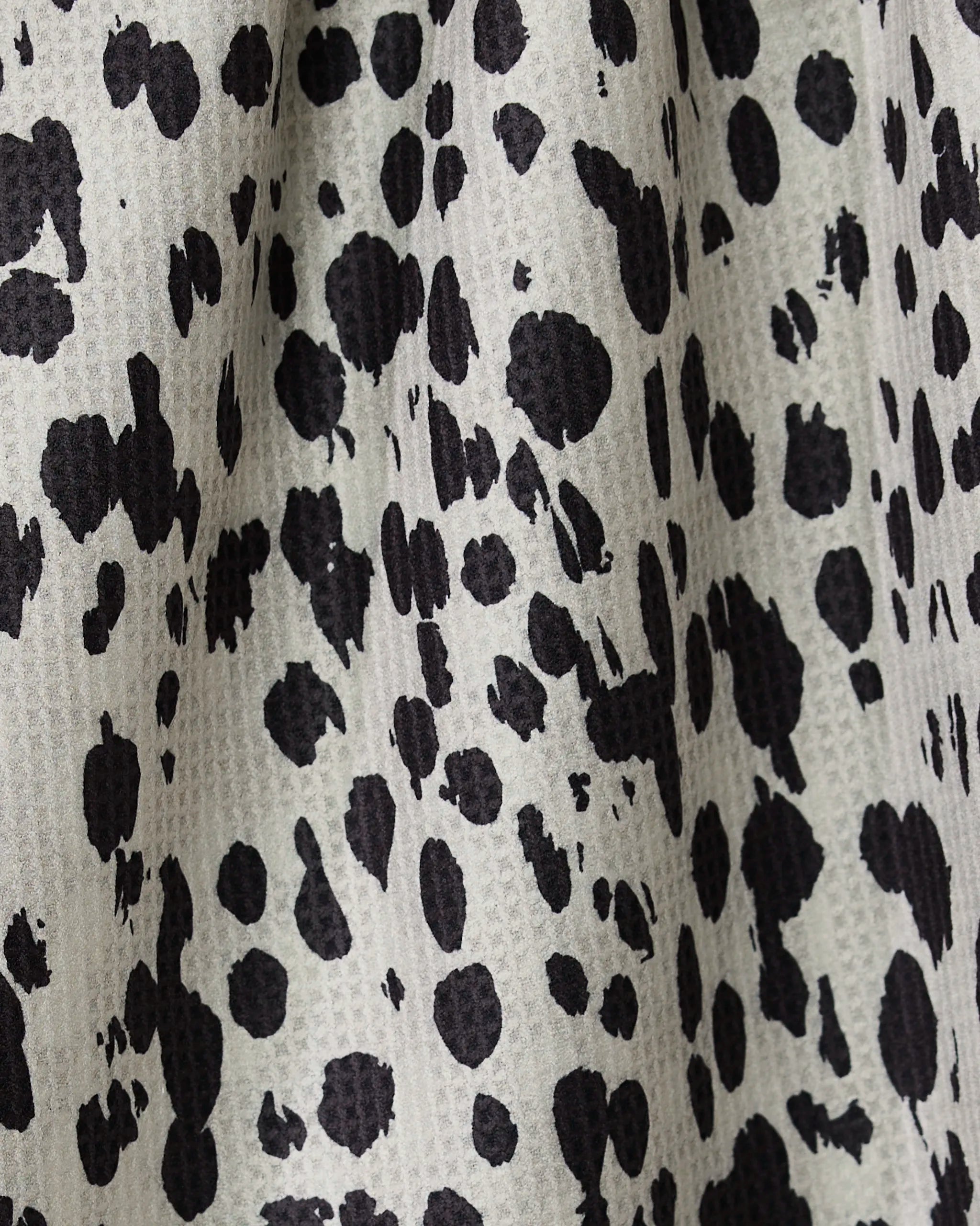 Close-up of Geometrys Cass recycled kitchen towel, showing a black and white Dalmatian-style spotted pattern with a lightly textured, woven surface and irregular black spots on a pale background.