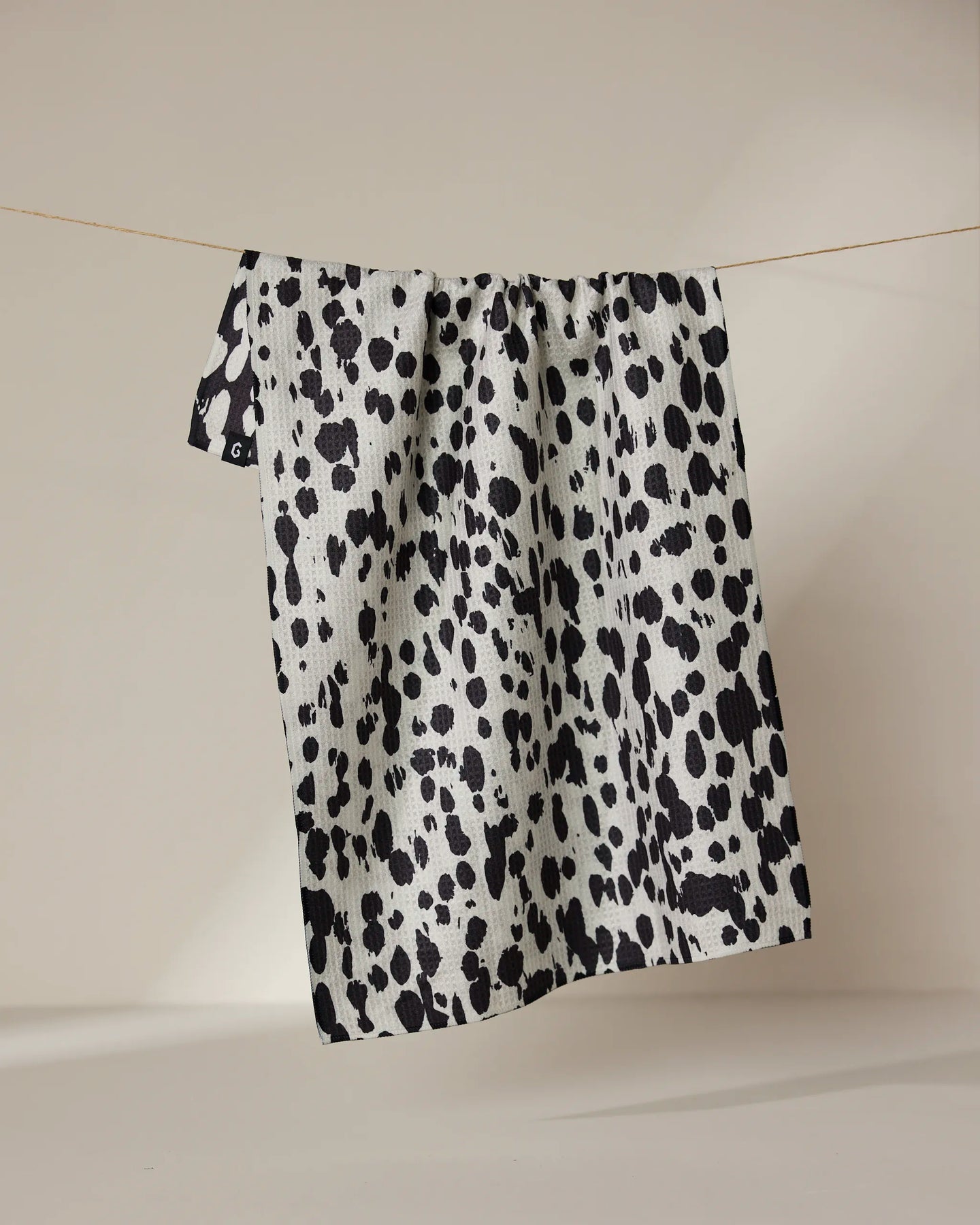 The Geometry Cass tea towel, featuring black and white spots and made with quick-dry fabric, hangs on a clothesline against a simple, light background.