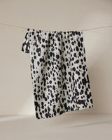 The Geometry Cass tea towel, featuring black and white spots and made with quick-dry fabric, hangs on a clothesline against a simple, light background.