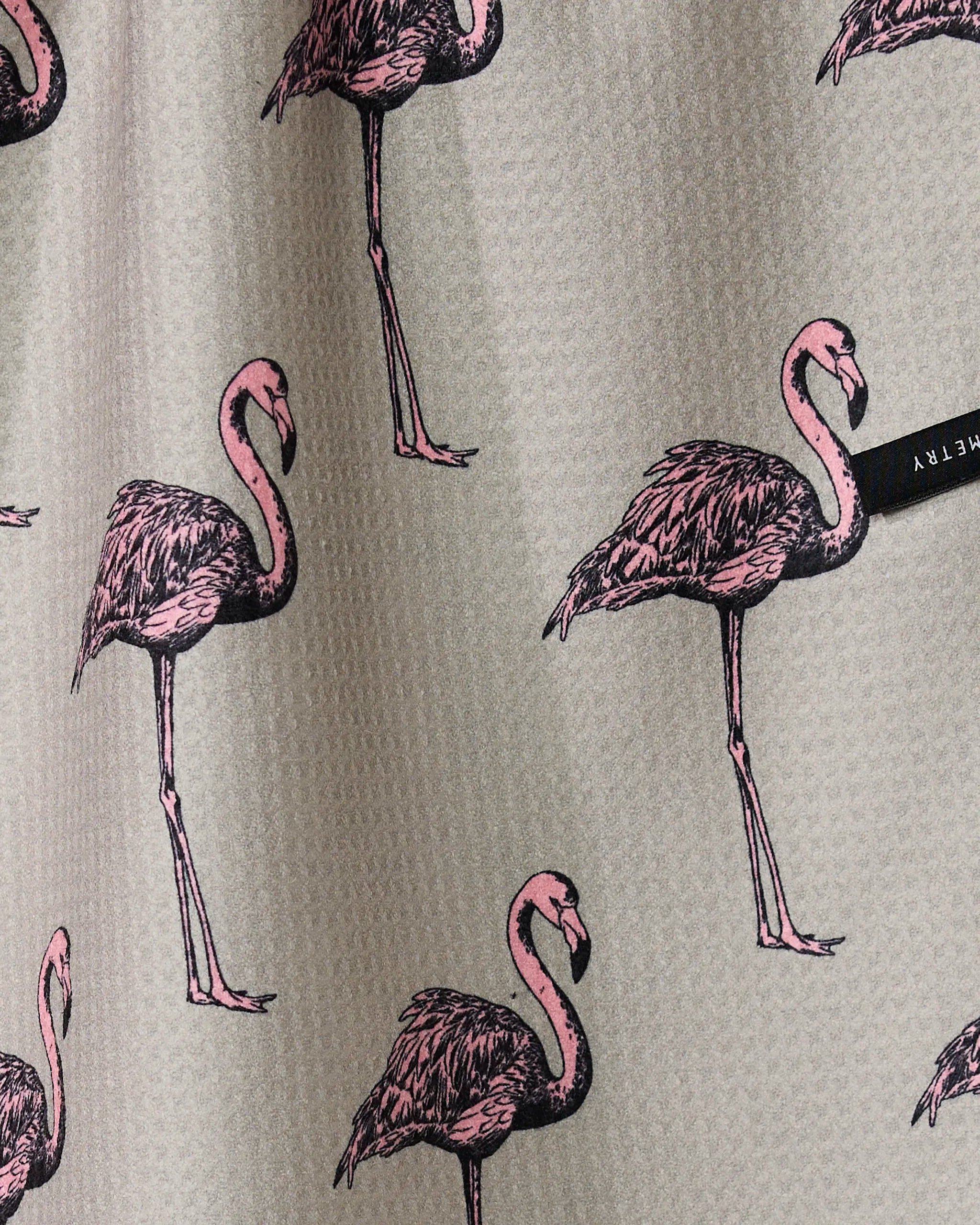 The Geometry Flamingo Dance tea towel features gray textured fabric with illustrated pink flamingos in various poses and a small black tag on the right side.