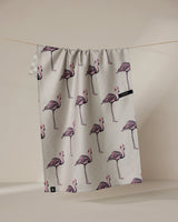 The Geometry Flamingo Dance tea towel, featuring a light gray color and pink flamingo pattern, dries quickly and hangs on a thin clothesline against a plain, light background.