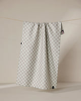 The Geometry Flamingo Dance double-sided tea towel, featuring a light gray and white checkered pattern, hangs on a thin clothesline against a beige background with subtle shadows.
