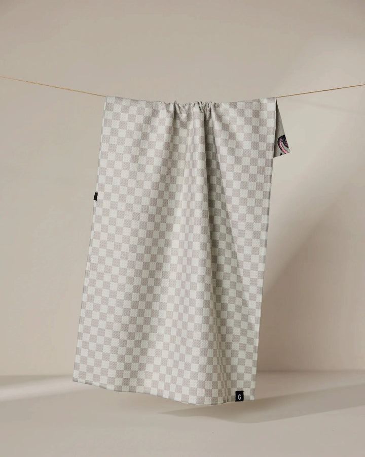 The Geometry Flamingo Dance double-sided tea towel, featuring a light gray and white checkered pattern, hangs on a thin clothesline against a beige background with subtle shadows.