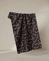 The Sweet Canes recycled kitchen towel by Geometry, featuring a red and white candy cane pattern on black, hangs on a string against a neutral background.