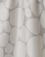 The Geometry Stone curtain is white with a subtle texture and features a light gray pattern of overlapping, irregular ovals and circles—resembling stones or pebbles, inspired by modern recycled kitchen towel designs.