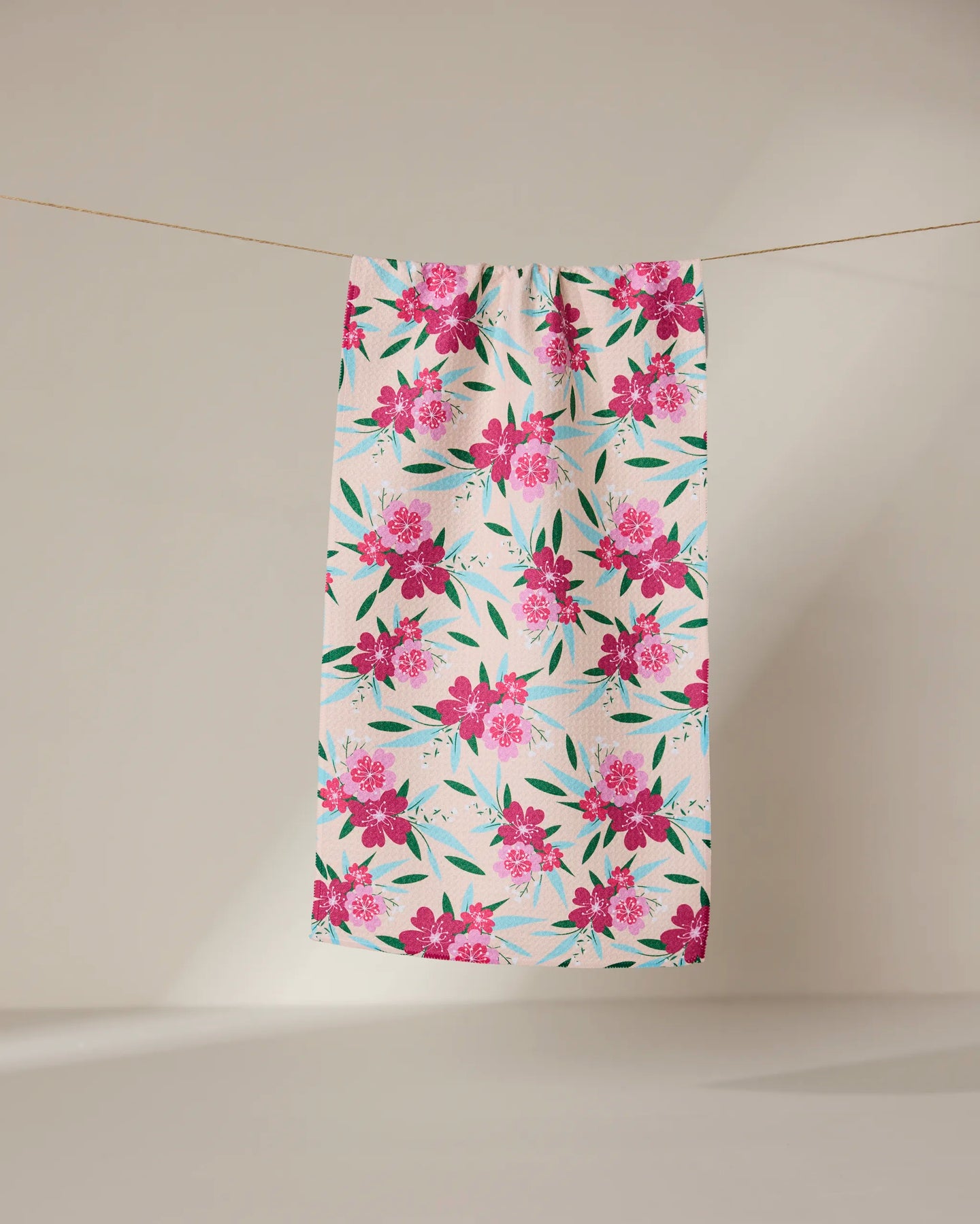 The GEOMETRY Sending Love bar towel features a white background with a bright pink floral pattern and green leaves. Made from ultra-absorbent fabric, it hangs on a clothesline against a neutral beige backdrop. Perfect for daily use.