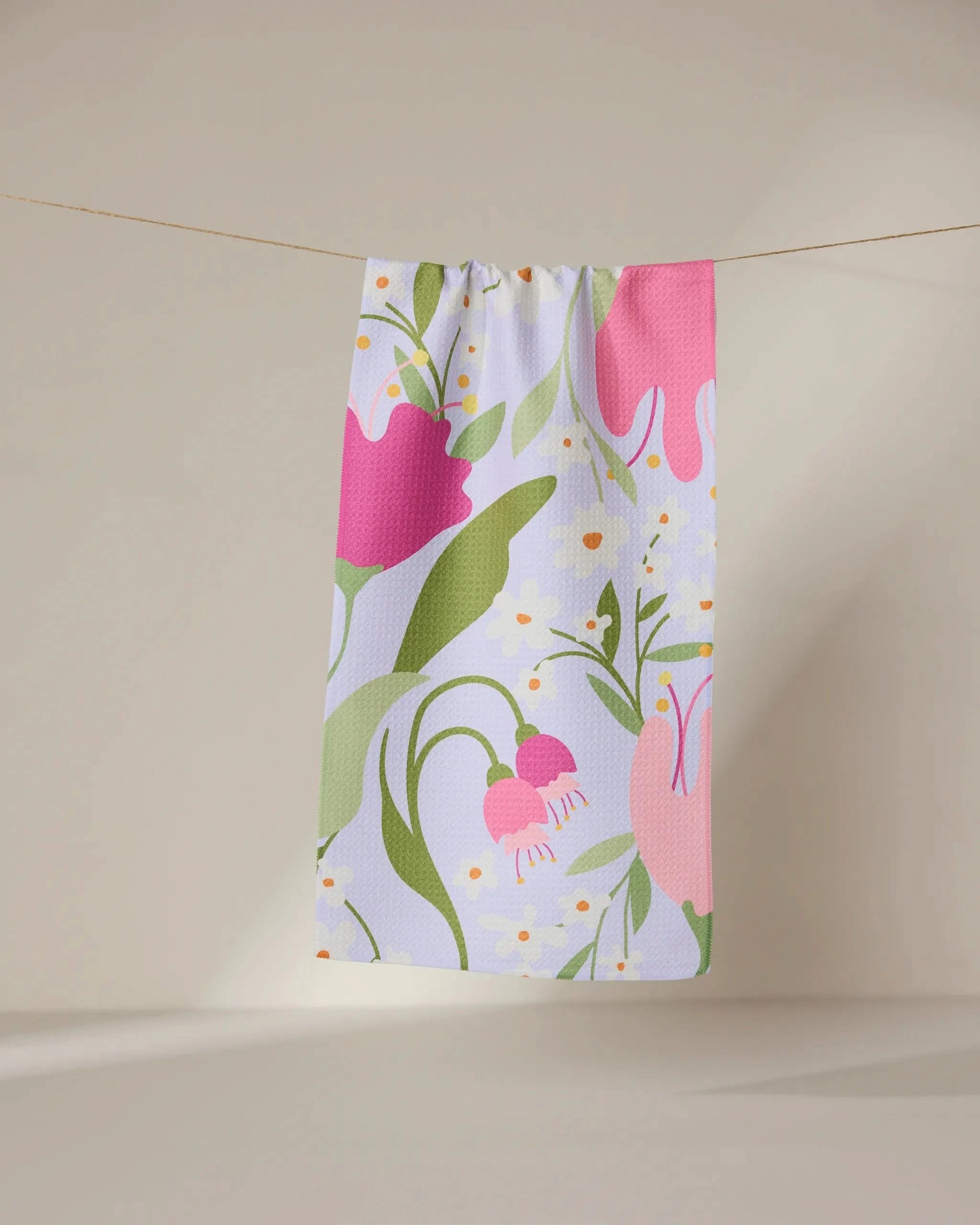 The GEOMETRY Thoughtful bar towel, crafted from recycled materials, features colorful pink, green, and yellow floral designs and hangs on a string against a neutral beige background.
