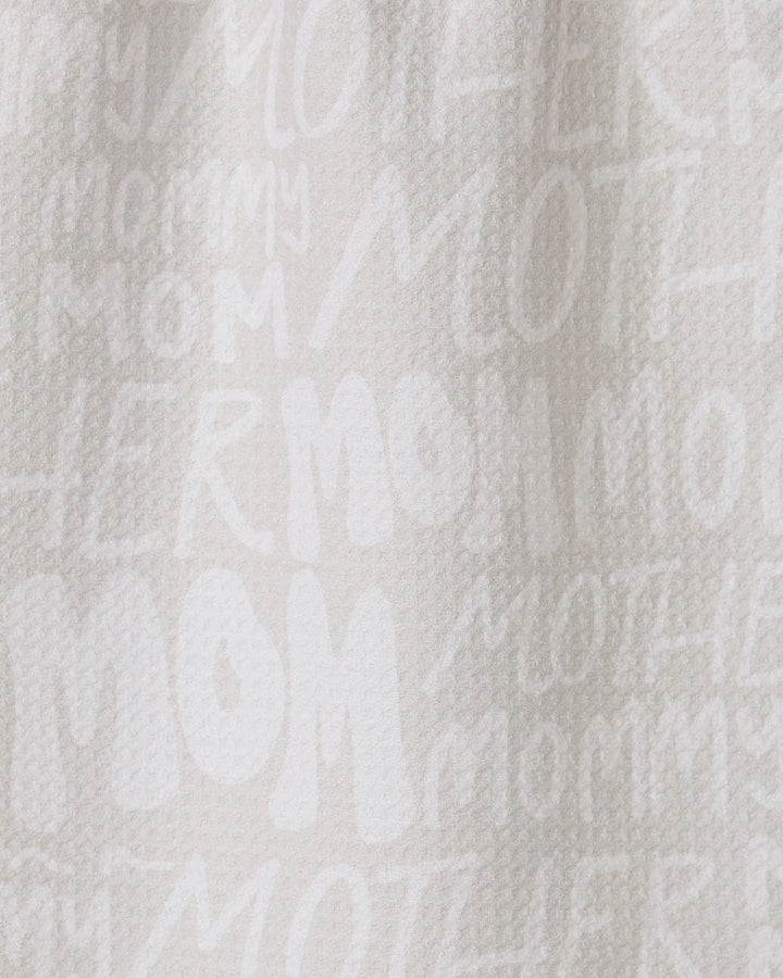 The GEOMETRY Mom bar towel is crafted from recycled white textured fabric, featuring “MOM,” “MOTHER,” and “MOMMY” in varied fonts and sizes printed subtly across its surface.