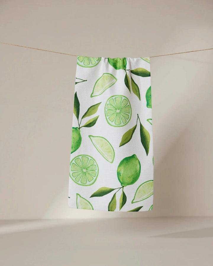 The GEOMETRY Lima kitchen towel, crafted from recycled materials and featuring green lime and leaf designs, hangs on a clothesline against a simple beige background.