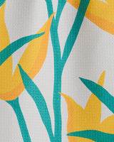 A close-up of the GEOMETRY Growth recycled kitchen towel, featuring a vibrant yellow flower print with teal leaves and stems on a textured white background.