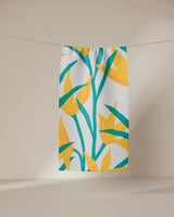 The GEOMETRY Growth towel, ultra-absorbent and white with vibrant yellow and green tropical leaf print, hangs on a clothesline against a neutral background.