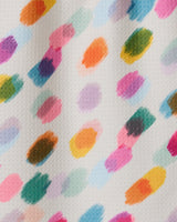 A close-up of GEOMETRY’s Downpour bar towel shows textured white fabric with colorful, irregular paint dabs in diagonal rows. Ultra-absorbent and made from recycled materials, it features bright orange, pink, green, purple, and blue accents.