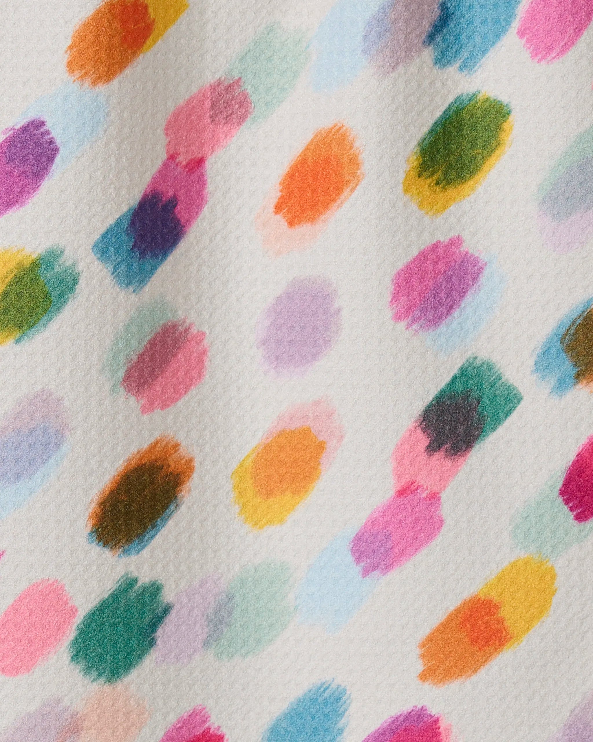 A close-up of GEOMETRY’s Downpour bar towel shows textured white fabric with colorful, irregular paint dabs in diagonal rows. Ultra-absorbent and made from recycled materials, it features bright orange, pink, green, purple, and blue accents.
