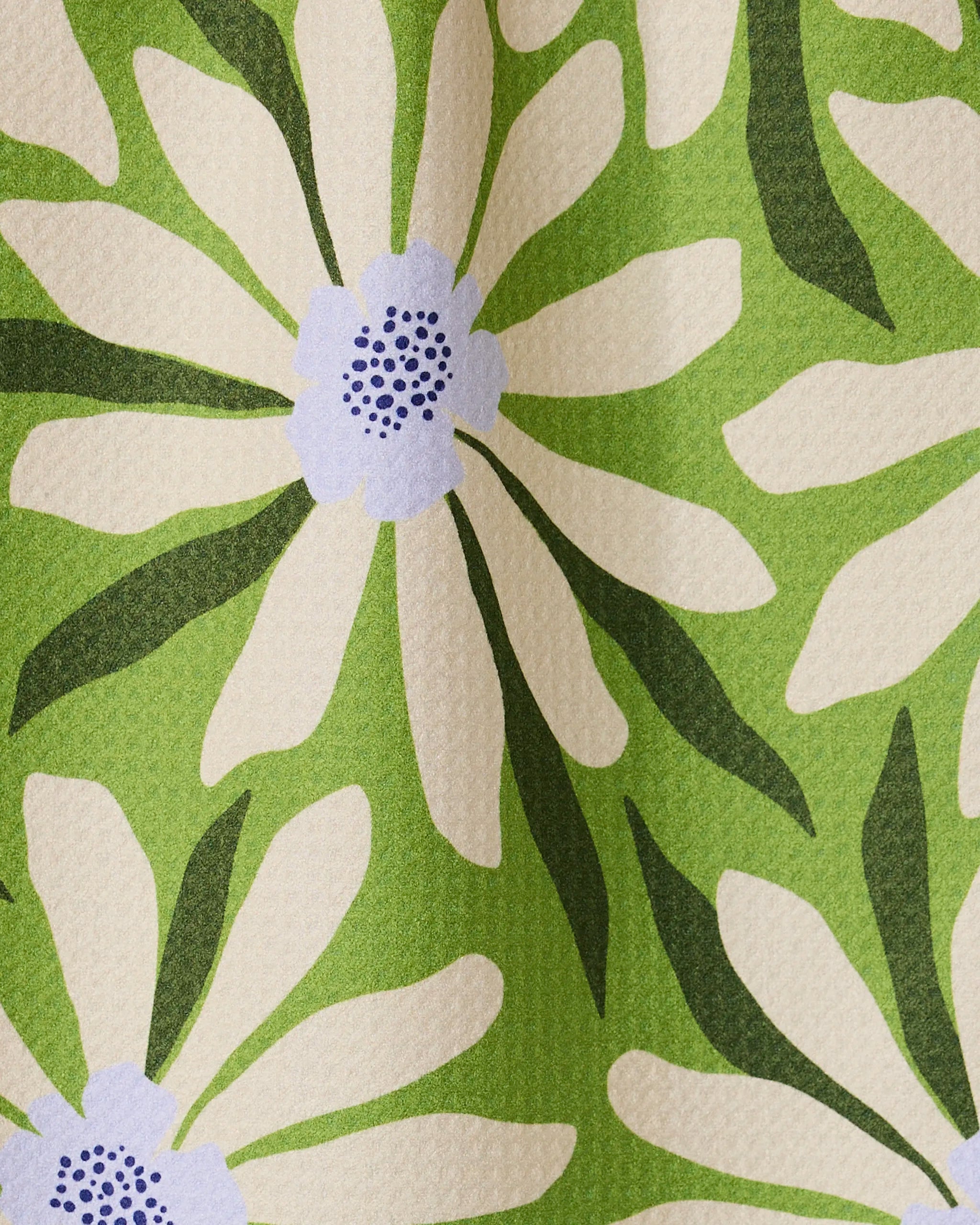 A close-up of the GEOMETRY Bliss and Bloom bar towel shows its ultra-absorbent, textured fabric featuring large white daisies with purple centers and green leaves on a light green background, displayed in soft folds.