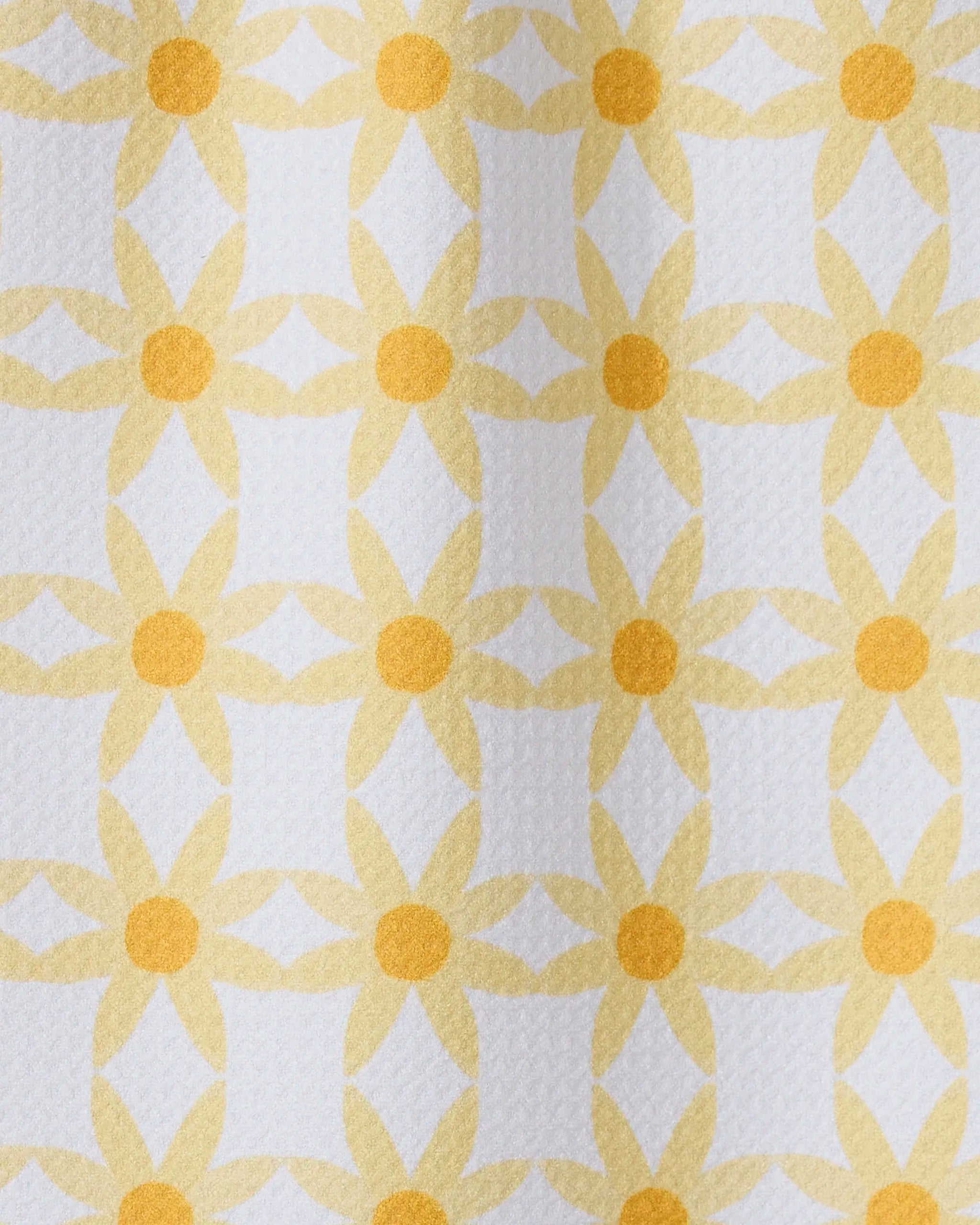 A close-up of GEOMETRYs Daisies recycled kitchen towel, showcasing a repeating yellow daisy-like geometric pattern on a white background.