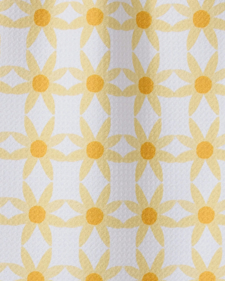 A close-up of GEOMETRYs Daisies recycled kitchen towel, showcasing a repeating yellow daisy-like geometric pattern on a white background.