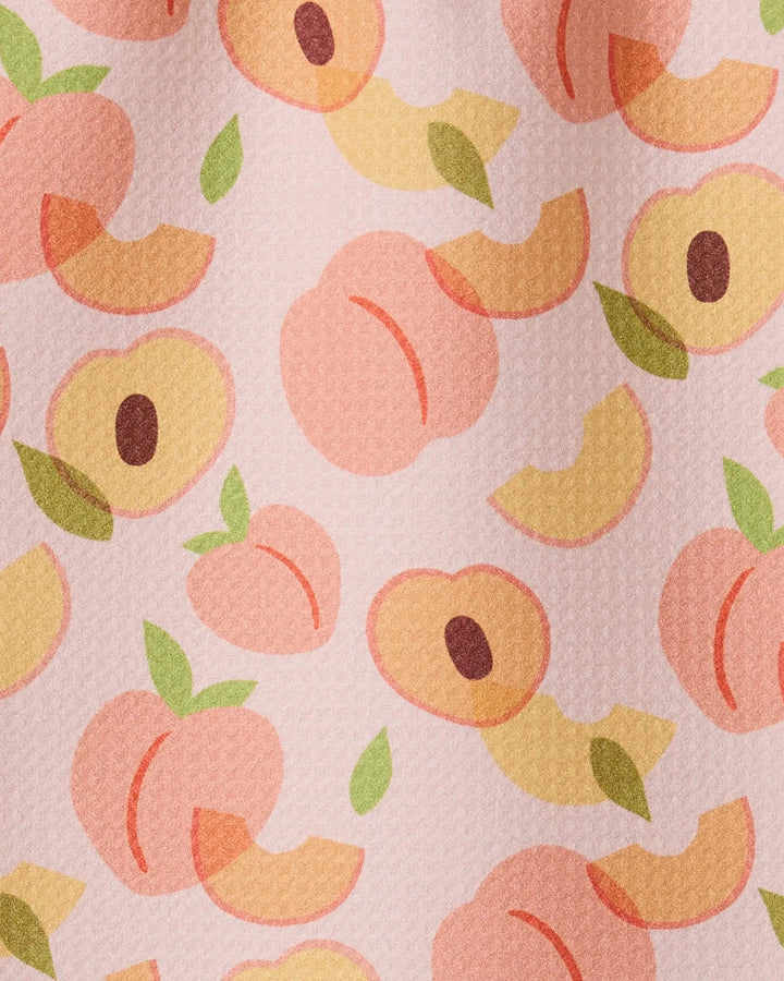 The GEOMETRY Peaches towel features a seamless design of whole and sliced peaches with green leaves on a textured light pink background, crafted from ultra-absorbent recycled materials.