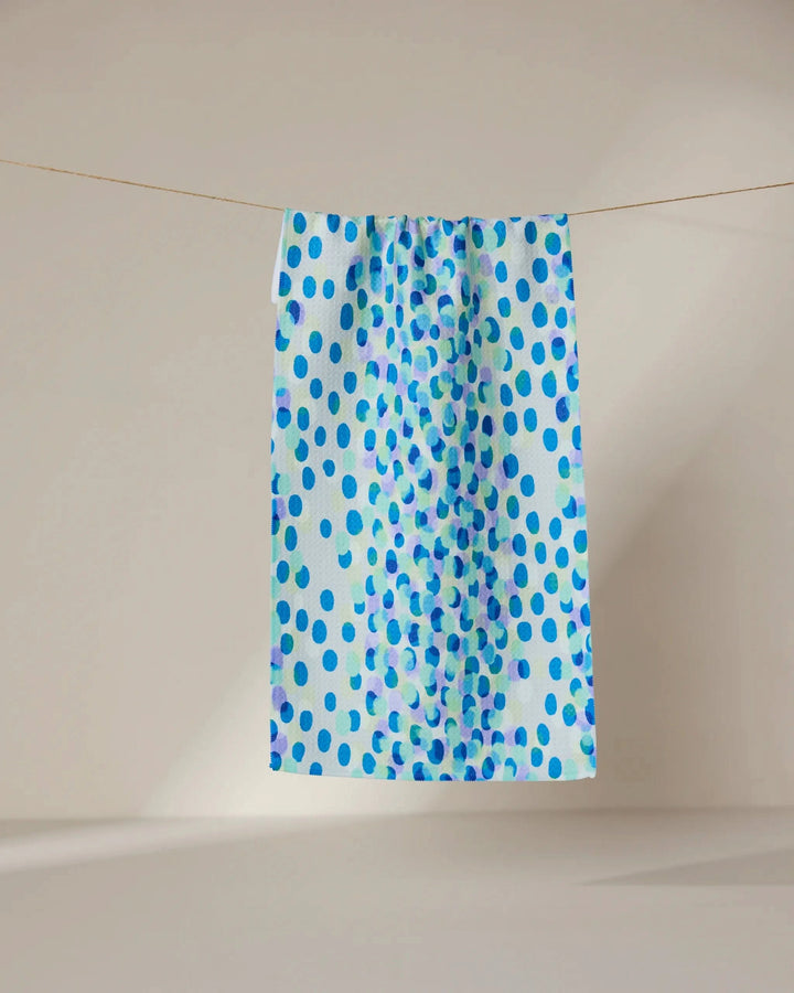 The GEOMETRY Spotty Summer towel, featuring a blue polka dot design and ultra-absorbent rectangular shape, hangs on a clothesline against a softly lit neutral background.