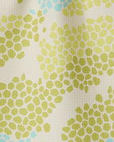 A close-up of GEOMETRY’s Geo Shell fabric shows clustered green and light blue irregular dots on a cream background, crafted from recycled materials and resembling abstract floral or pebble shapes.