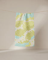 The GEOMETRY Geo Shell towel, featuring a patterned ultra-absorbent design, hangs on a clothesline with sunlight casting soft shadows on the neutral wall and floor in the background.