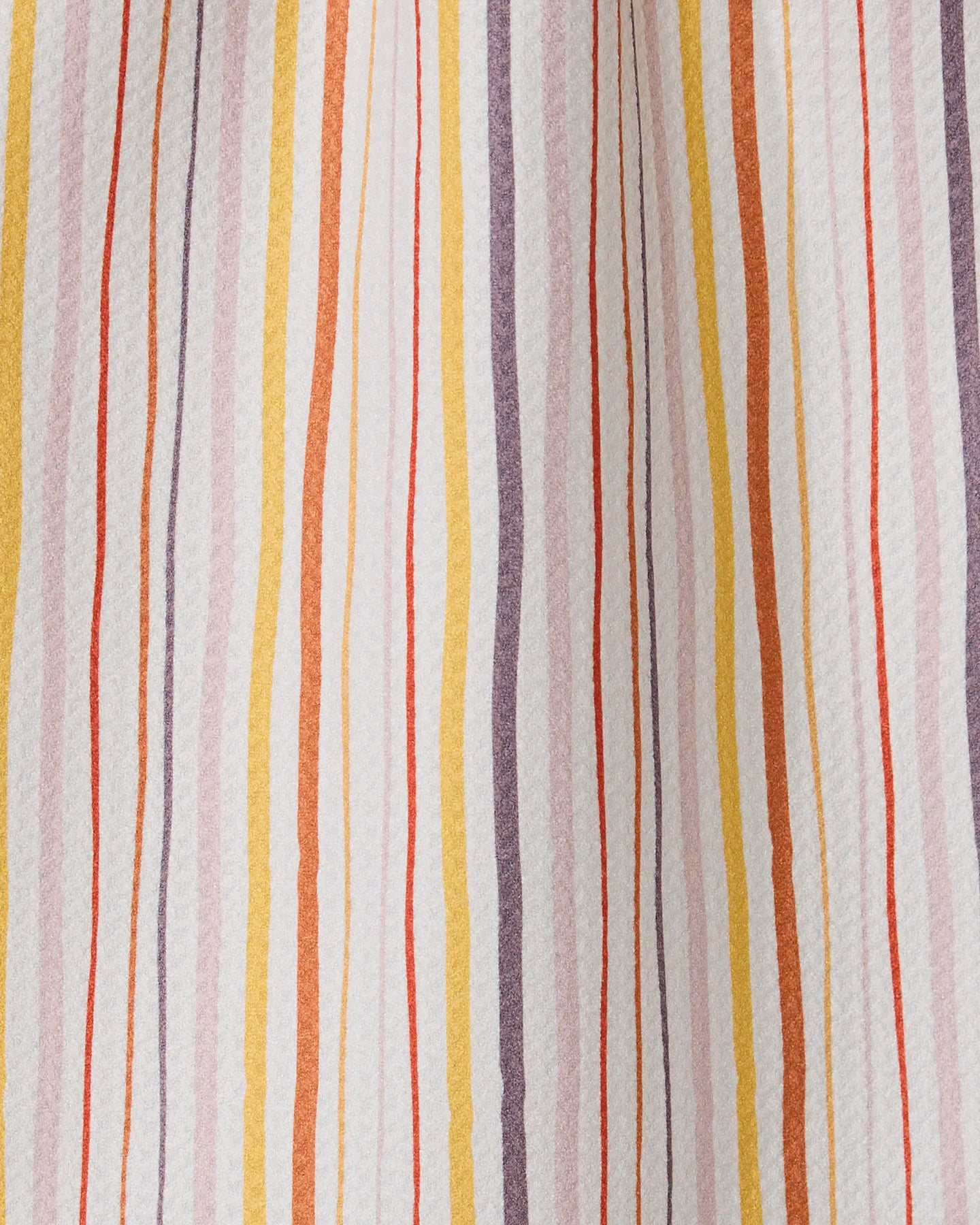 A close-up of Stripe Season by GEOMETRY: fabric crafted from recycled materials, featuring vertical wavy stripes in orange, yellow, purple, and red on a white background with varied thickness and spacing.