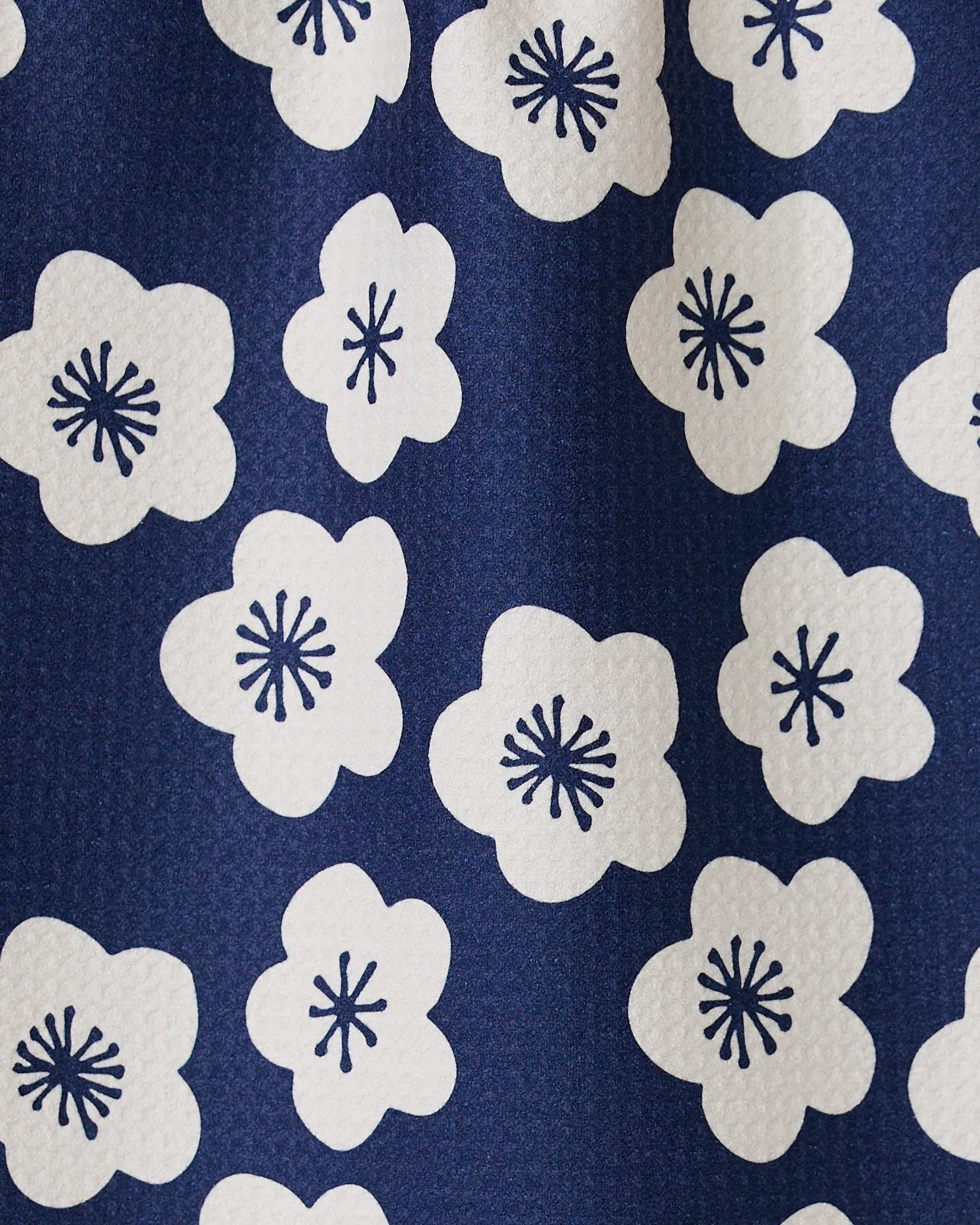 A close-up of GEOMETRYs Every Sunday kitchen towel showcases blue fabric with white floral patterns and dark blue centers. Its slightly pebbled texture adds style, while ultra-absorbency makes it perfect for daily use.
