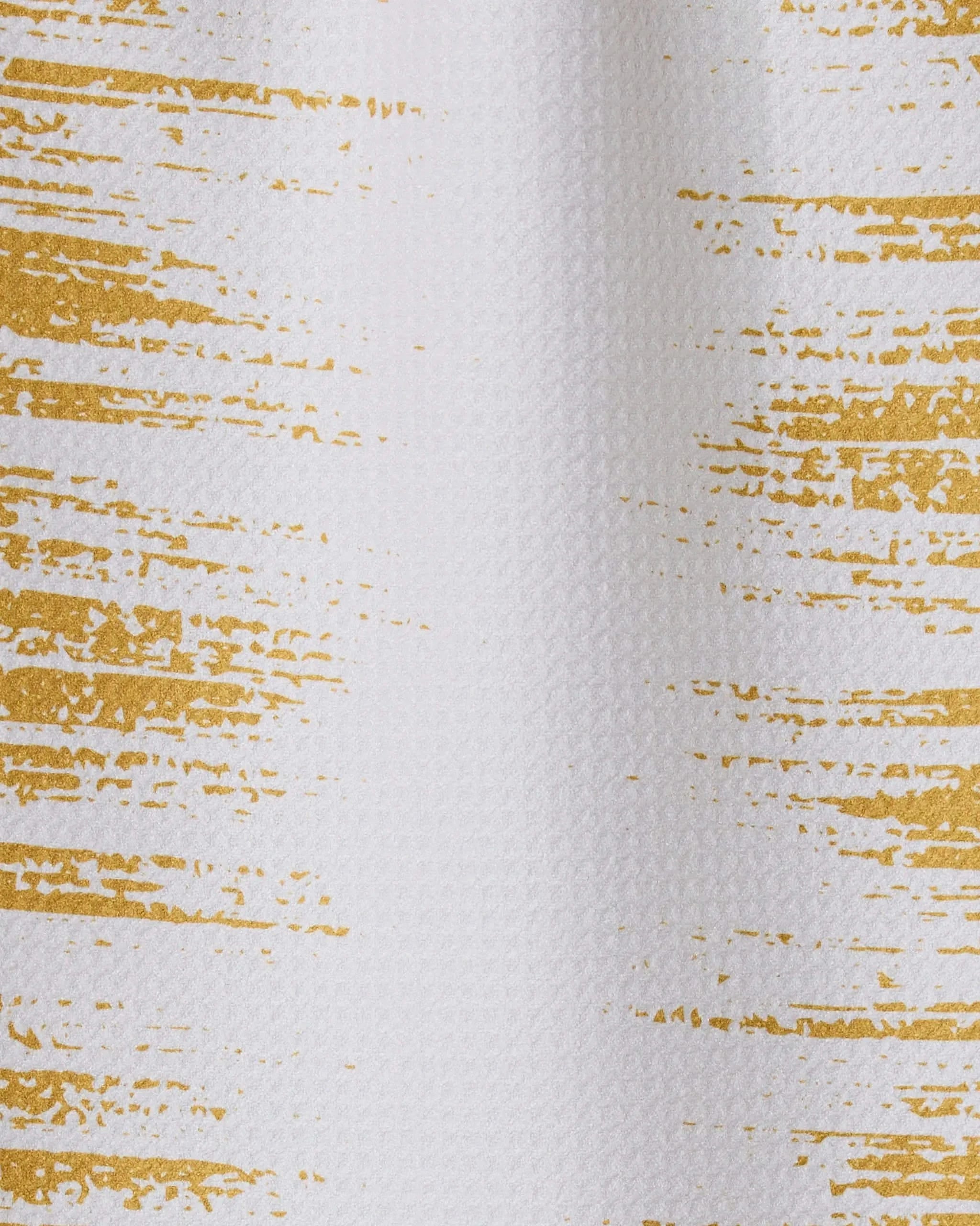 Worn Gold by GEOMETRY features white textured fabric with uneven horizontal gold brushstrokes. Made from recycled materials, its modern design has a subtle metallic gold sheen for a chic, eco-friendly style.