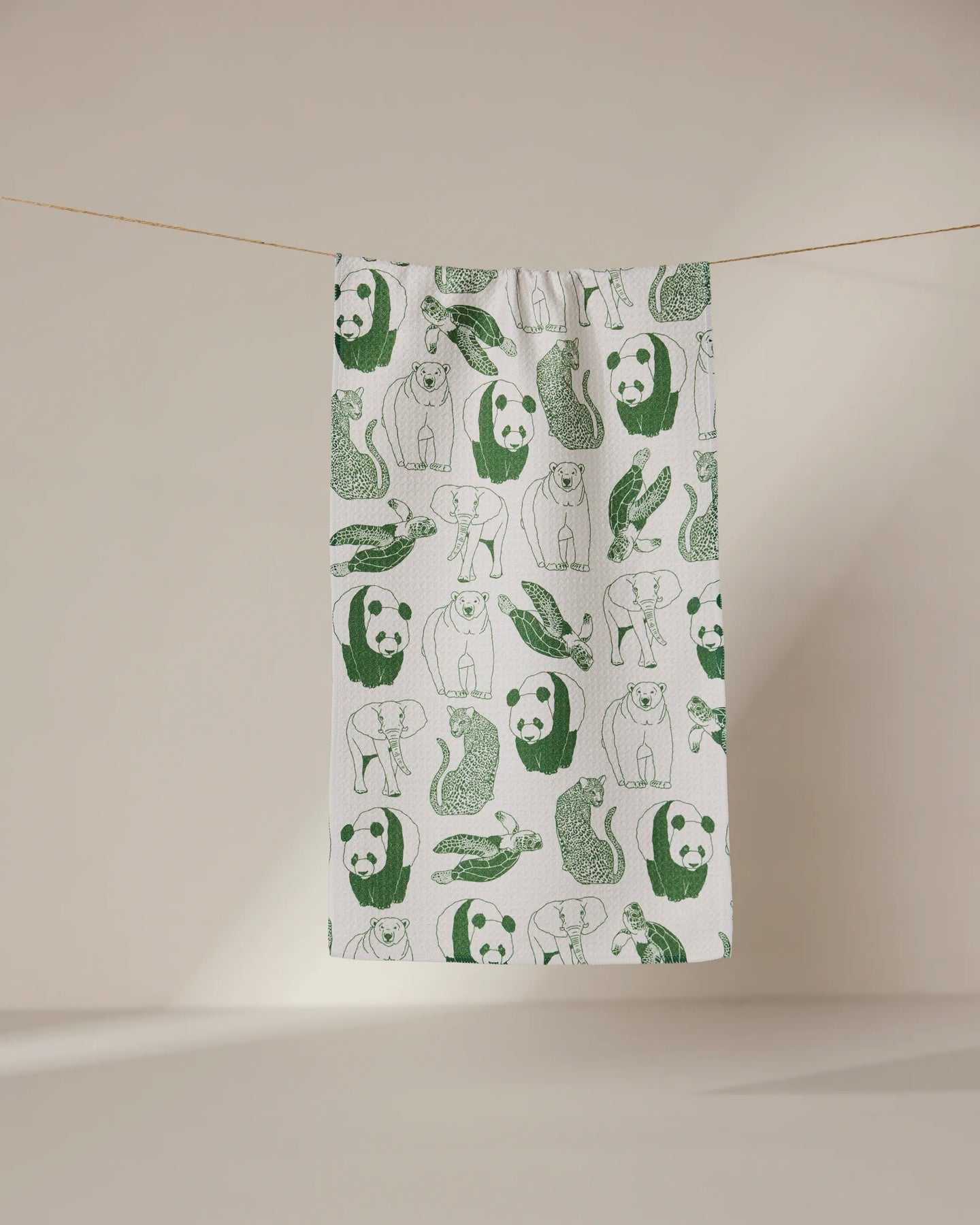 The GEOMETRY Endangered towel, featuring green illustrations of pandas, bears, walruses, and seals on ultra-absorbent white fabric, hangs on a line against a neutral background.